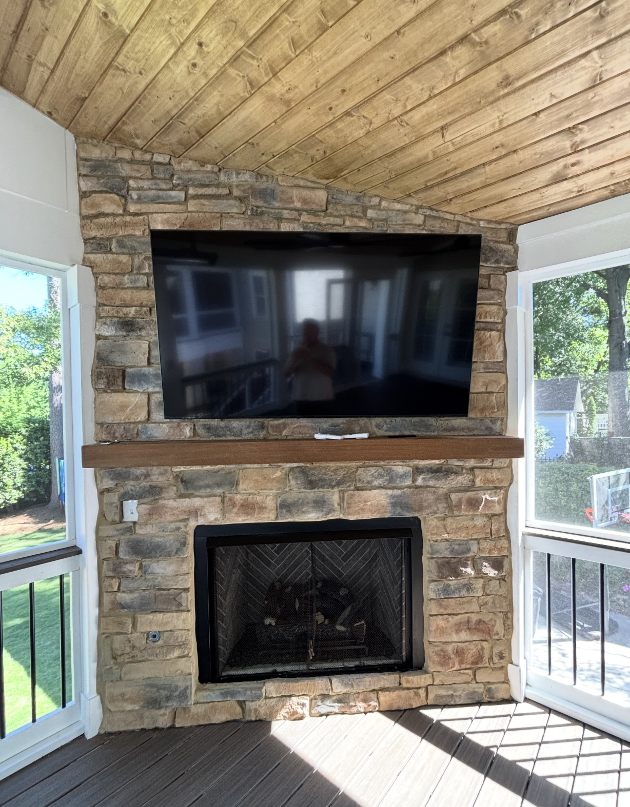 Stone gas fireplace with TV mounted above and wood mantel