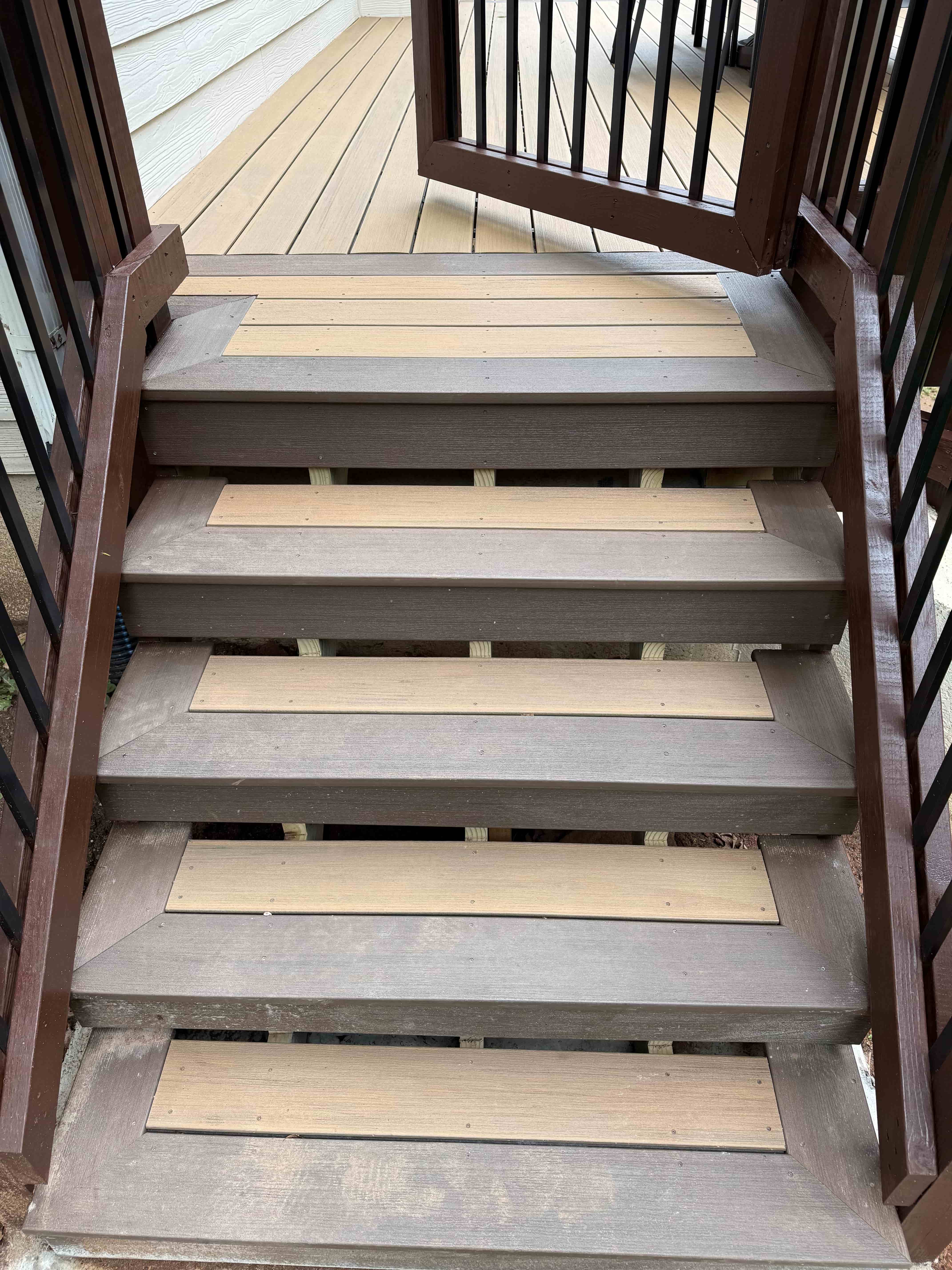 Two-tone composite deck stairs with tan treads, brown frame, and black balusters