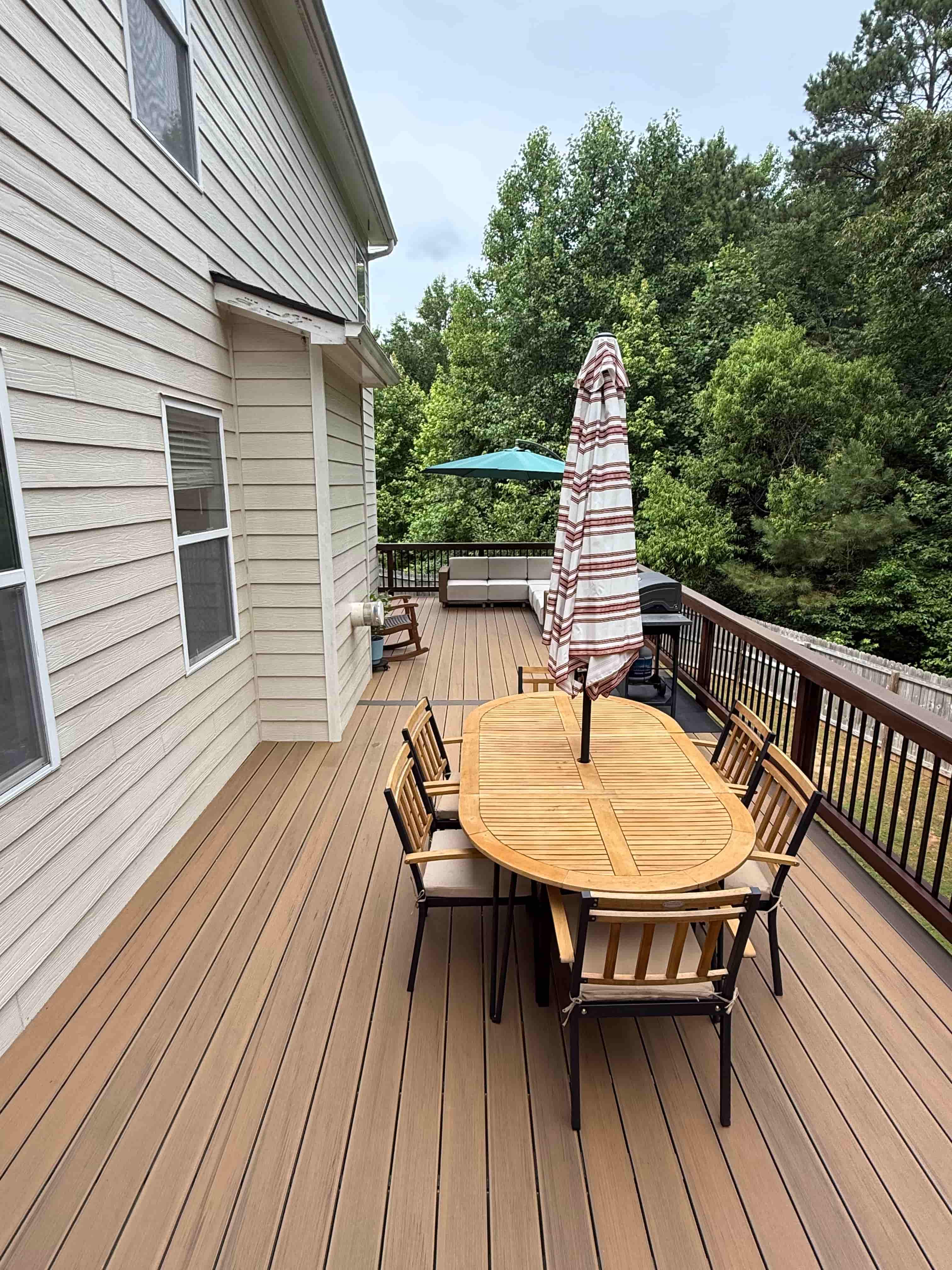 Composite deck with teak dining table, umbrella, and wooded backyard views
